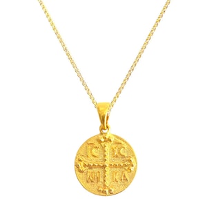 Op de afbeelding: Een gouden ketting met een ronde hanger met een kruis en het woord "NIKA" in Griekse letters.