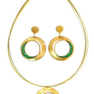 May include: A gold-toned jewelry set featuring a necklace and matching earrings. The necklace has a double-strand chain with a circular pendant. The earrings are also circular. Each piece has a green accent within the circular design.