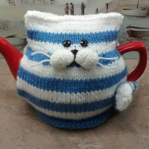 May include: Blue and white striped knitted teapot cosy shaped like a cat with black eyes and white whiskers.