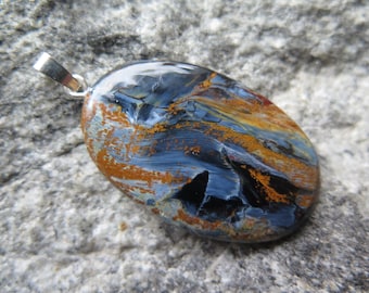 May include: A silver pendant with a blue and gold tiger's eye stone. The stone is oval shaped and has a swirling pattern.