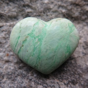Può includere: Una pietra verde a forma di cuore con venature bianche e una superficie liscia e lucida.