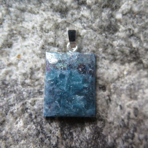Peut inclure: Un pendentif en argent avec une pierre précieuse rectangulaire bleue et verte. La pierre précieuse a une finition scintillante et irisée.