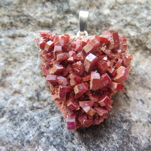 Peut inclure: Un pendentif en cristal rouge avec une bélière en argent. Le cristal est un amas de petits cristaux cubiques rouges.