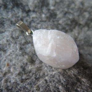 May include: A pale pink crystal pendant with a silver bail. The crystal is rough and has a natural, organic shape.