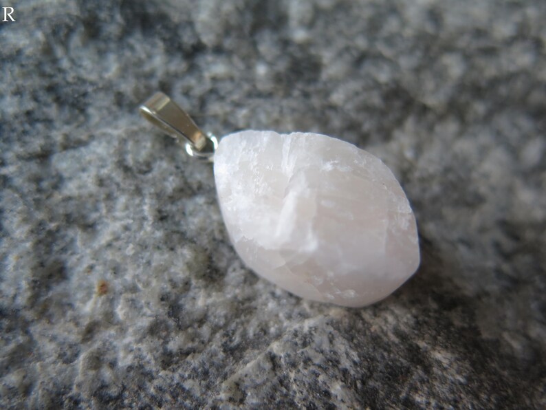 May include: A pale pink crystal pendant with a silver bail. The crystal is rough and has a natural, organic shape.