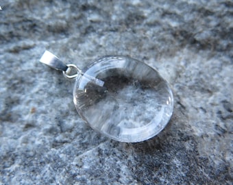 May include: A clear crystal pendant with a silver bail. The crystal is round and has a smooth, polished surface.