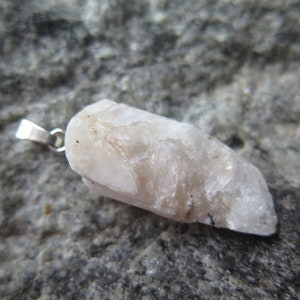 May include: A white, raw, crystal pendant with a silver bail. The crystal has a rough, natural texture and is attached to a silver chain.