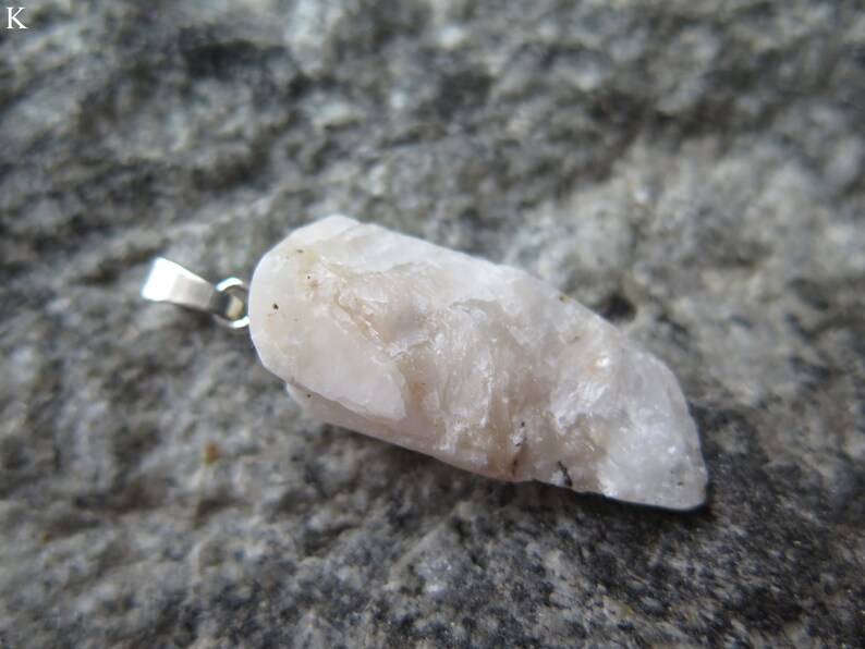 May include: A white, raw, crystal pendant with a silver bail. The crystal has a rough, natural texture and is attached to a silver chain.
