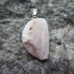 May include: A pale pink, irregularly shaped stone pendant with a silver bail. The stone has a rough, natural texture and subtle red veins.