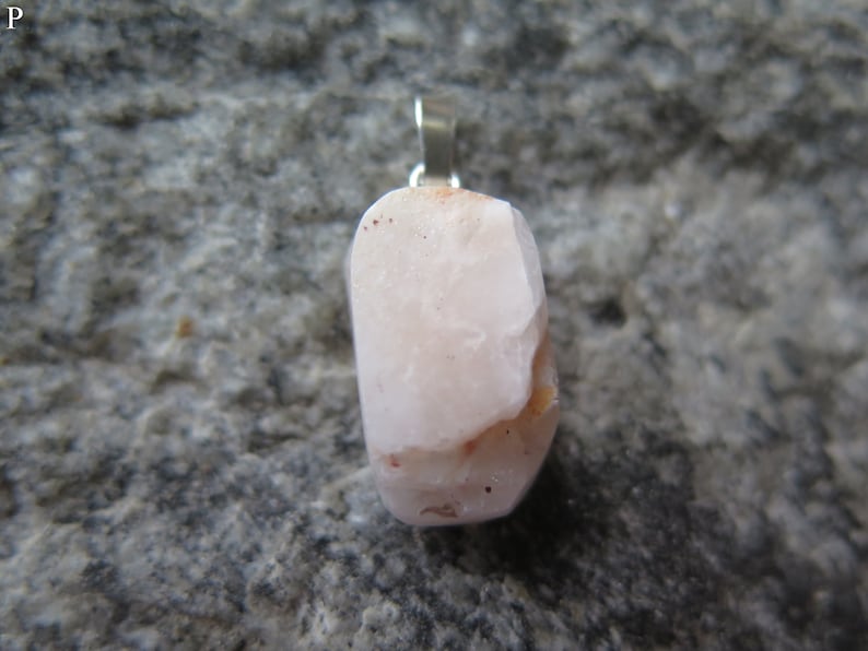 May include: A pale pink, irregularly shaped stone pendant with a silver bail. The stone has a few reddish-brown inclusions.
