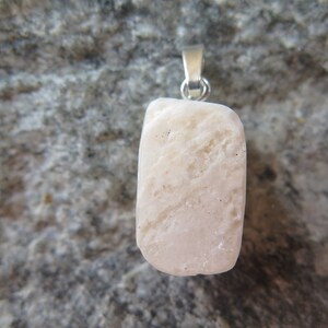 May include: A white, rough-textured stone pendant with a silver bail. The pendant is hanging against a gray, textured background.