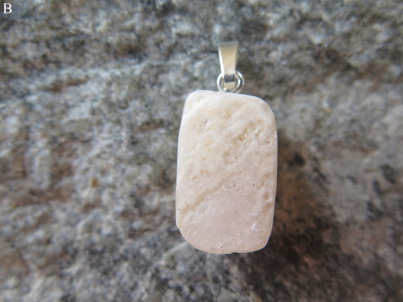May include: A white, rough-textured stone pendant with a silver bail. The pendant is hanging against a gray, textured background.