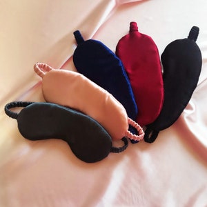 Five real silk eye masks in deep grey, pale pink, navy blue, deep red and black against a pale pink silk background