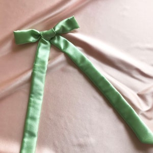 A pale mint green silk ribbon tied into a bow against a pale pink silk background
