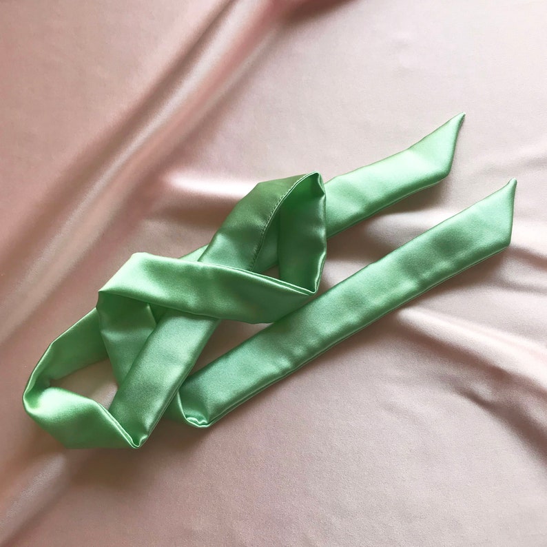 A pale mint green silk ribbon laid randomly against a pale pink silk background