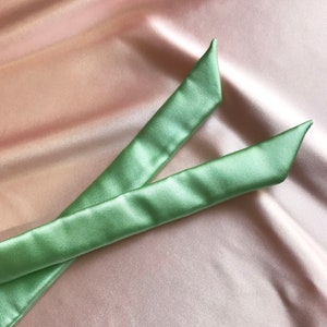 The two ends of a pale mint green silk ribbon against a pale pink silk background