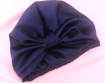 May include: A navy blue satin sleep cap with a large bow on top. The cap is designed to protect hair while sleeping.
