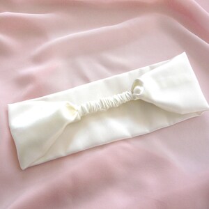 A white silk headband with elasticated silk covered strap against a pale pink silk background