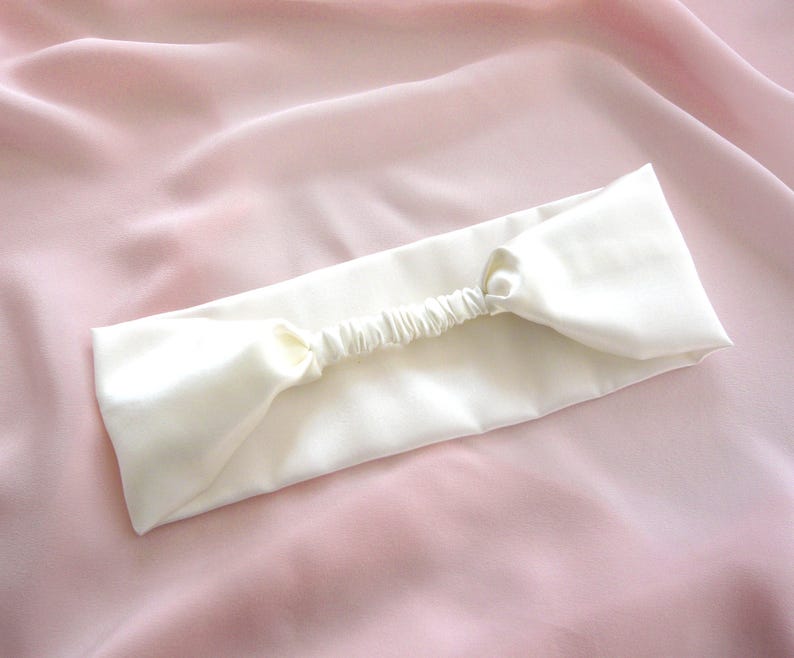 A white silk headband with elasticated silk covered strap against a pale pink silk background