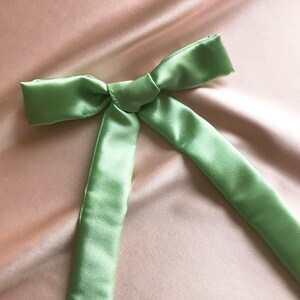 A pale mint green silk ribbon tied into a bow against a pale pink silk background