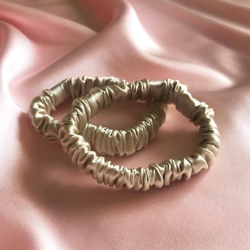 Two golden beige champagne  silk hair elastics on a pale pink background