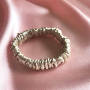 A golden beige champagne  silk hair elastics on a pale pink background