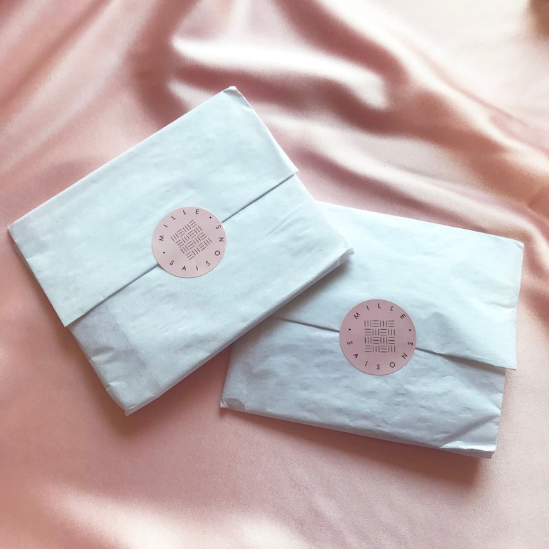 Two white tissue paper packages sealed with a pink Mille Saisons branded sticker on a pale pink silk background