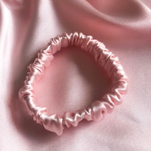 Puede incluir: Un scrunchie de satén rosa para el cabello. El scrunchie está hecho de un tejido suave y liso y está diseñado para ser suave con el cabello.