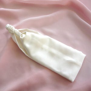 A white silk headband with elasticated silk covered strap against a pale pink silk background