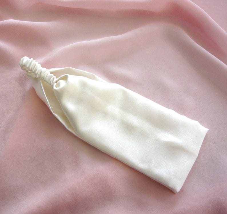 A white silk headband with elasticated silk covered strap against a pale pink silk background