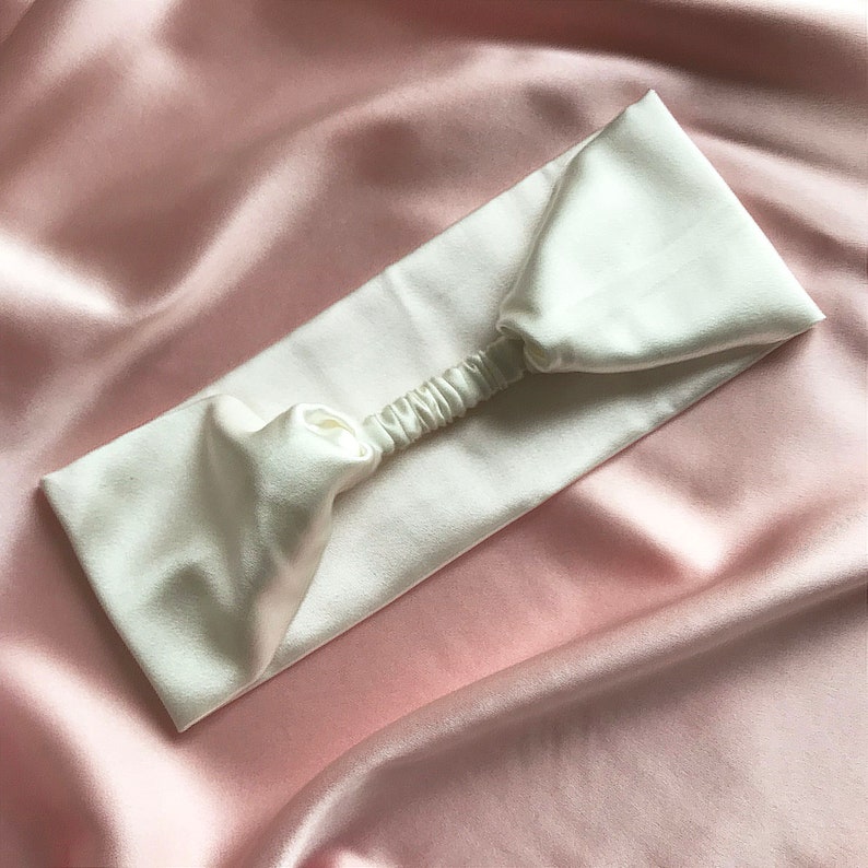 A white silk headband with elasticated silk covered strap against a pale pink silk background