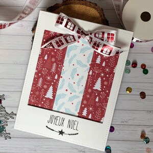 May include: A white Christmas card with a rectangular cutout, featuring a red and white patterned design and a bow with gift box ribbon. The card reads "JOYEUX NOEL" in black script, with a star and decorative elements.