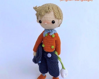 Könnte beinhalten: Häkelanleitung für eine niederländische Jungenpuppe mit orangefarbenem Pullover, blauer Hose und einer weißen Blume. Die Anleitung ist in englischer Sprache und als PDF-Download erhältlich.