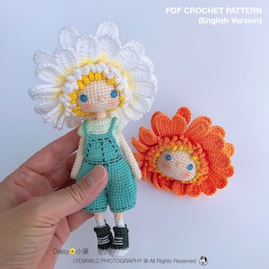 May include: Crochet pattern for a daisy doll with a yellow face, blue eyes, and a white daisy hat. The doll is wearing a green and blue overall outfit and black shoes. The pattern is available in PDF format.