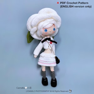 May include: A white crocheted doll with blue eyes and a white crocheted flower hat. The doll is wearing a white crocheted dress with a pink trim and a black crocheted purse. The doll is standing on a light blue background. The text "Camellia 小茶" is at the bottom of the image.