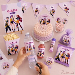 May include: A party decoration set featuring the name GIADA 5 ANNI, including a cake topper, popcorn box, water bottle labels, bubble wand, snack bag, and bunting. The items display a graphic of three animated characters in colorful outfits.