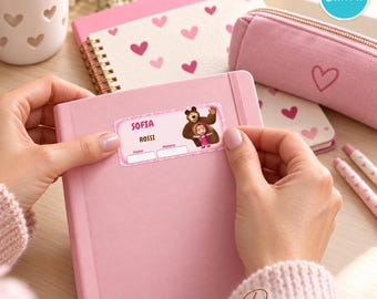 May include: A rectangular pink adhesive label featuring the cartoon characters Masha and the Bear, with the printed text SOFIA ROSSI, Classe, and Materia. The label is being applied to a solid pink notebook, surrounded by stationery items.