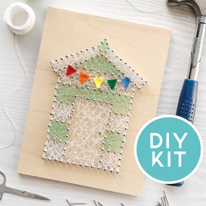 May include: A DIY string art kit depicting a house design with colourful pennants. The house is crafted with white string on a wooden board. The image includes a hammer, scissors, nails, and the text "DIY KIT".