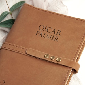K&ouml;nnte beinhalten: Ein braunes Lederjournal mit einer personalisierten Inschrift, die "Oscar Palmer" und "Pray with Love" lautet. Das Journal hat einen Lederriemenverschluss mit Messingakzenten.