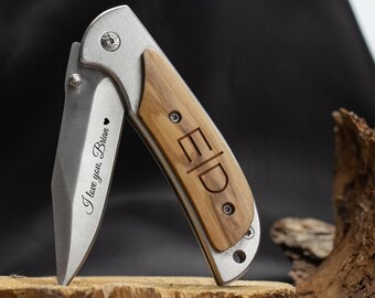 May include: A folding pocket knife with a stainless steel blade and a wooden handle. The blade is engraved with "I love you, Brian" and the handle has the initials "ED". The knife is open, displaying the blade, and rests on a wooden surface.