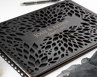May include: Black wooden guest book with a spiral binding and a cut-out design of leaves and flowers. The book is personalized with the names "JOSIE & ARTHUR" and the date "August 15, 2024".