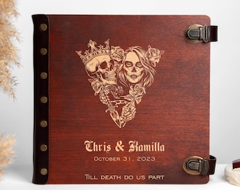 May include: A wooden photo album with a brown leather spine and metal clasps. The front cover features a gold engraved design of a skull and a woman with a sugar skull makeup, surrounded by roses. The text "Chris & Kamilla October 31, 2023 Till Death Do Us Part" is also engraved on the front cover.