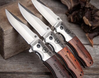 May include: Four pocket knives with wooden handles. The handles are engraved with the words "Best Man", "Groomsmen", and "Groomsmen".