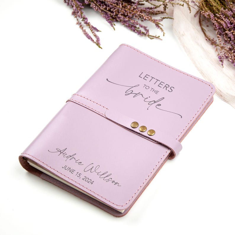 Op de afbeelding: Een lavendelkleurig lederen dagboek met de tekst "Letters to the Bride" en "Audrie Willson June 15, 2024" gegraveerd op de voorkant.