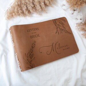 Pode incluir: Um di&aacute;rio encadernado em couro castanho com o texto "Cartas para a Noiva" e um design floral. O di&aacute;rio &eacute; personalizado com o nome "Melanie" e a data "08.15.2024".