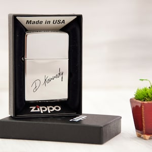 May include: Silver Zippo lighter in a black box with the inscription "D. Kennedy" and the words "Made in USA" on the box. The lighter is in a black box with the Zippo logo.