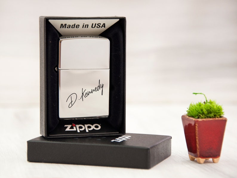 May include: Silver Zippo lighter in a black box with the inscription "D. Kennedy" and the words "Made in USA" on the box. The lighter is in a black box with the Zippo logo.