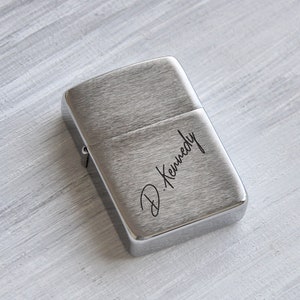 May include: Silver lighter with a brushed finish and the name "D. Kennedy" engraved on the front.