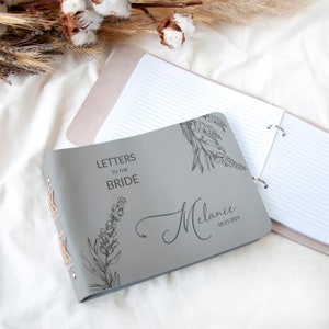 Pode incluir: Di&aacute;rio de couro cinza com o texto "Cartas para a noiva" e um design floral. O di&aacute;rio &eacute; personalizado com o nome "Melanie" e a data "08.15.2024".
