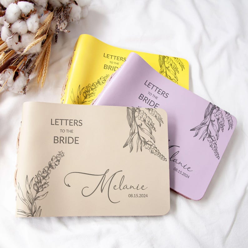 Pode incluir: Tr&ecirc;s di&aacute;rios bege, roxo e amarelo com o texto "Cartas para a noiva" e um design floral. Os di&aacute;rios s&atilde;o personalizados com o nome "Melanie" e a data "08.15.2024".